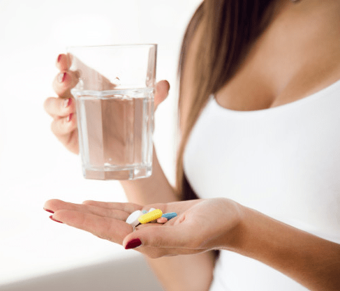Woman holding a glass of water and colorful pills